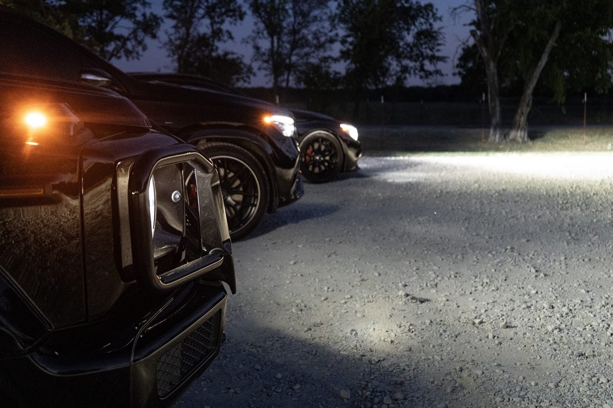 Three vehicles parked at dusk with their headlights on